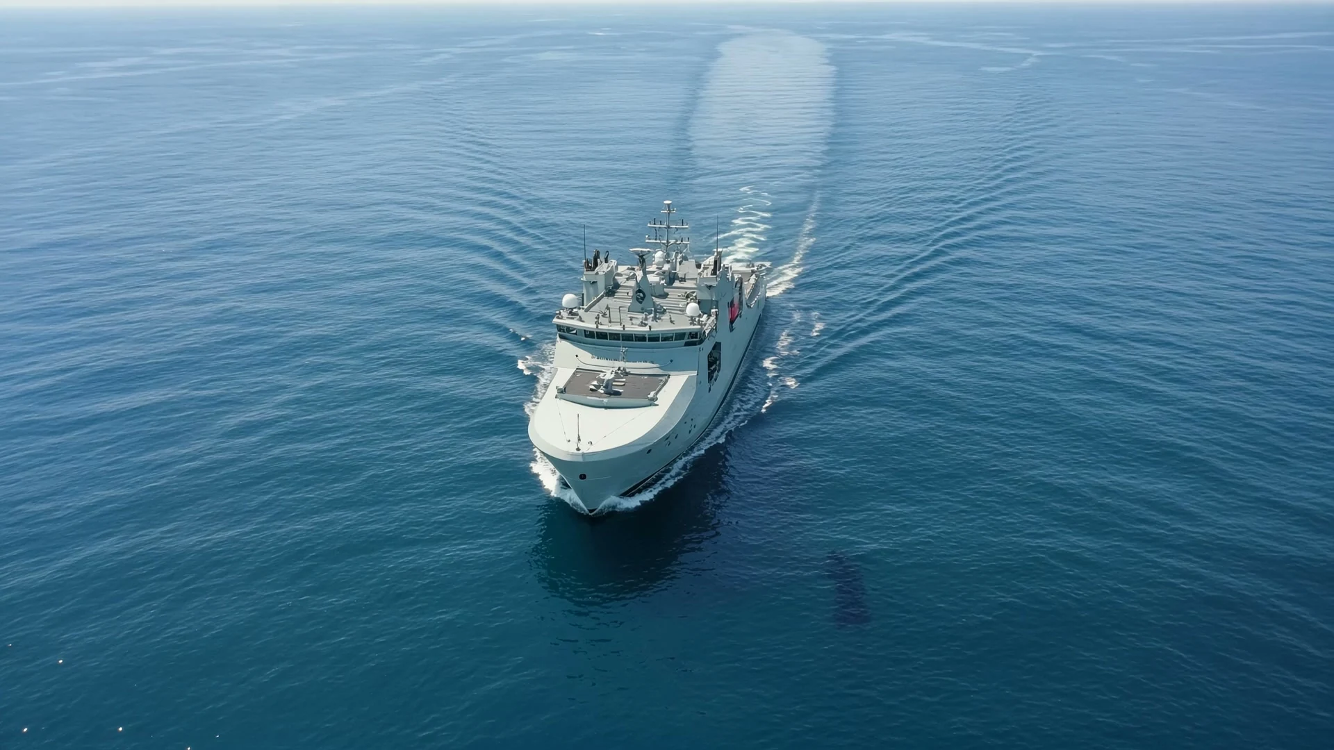 An aerial view of a naval vessel underway, leaving a wake across open water.